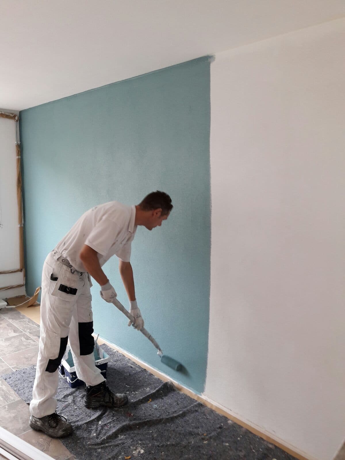 Schilder rolt een wand met Renovlies in een blauwgroene kleur